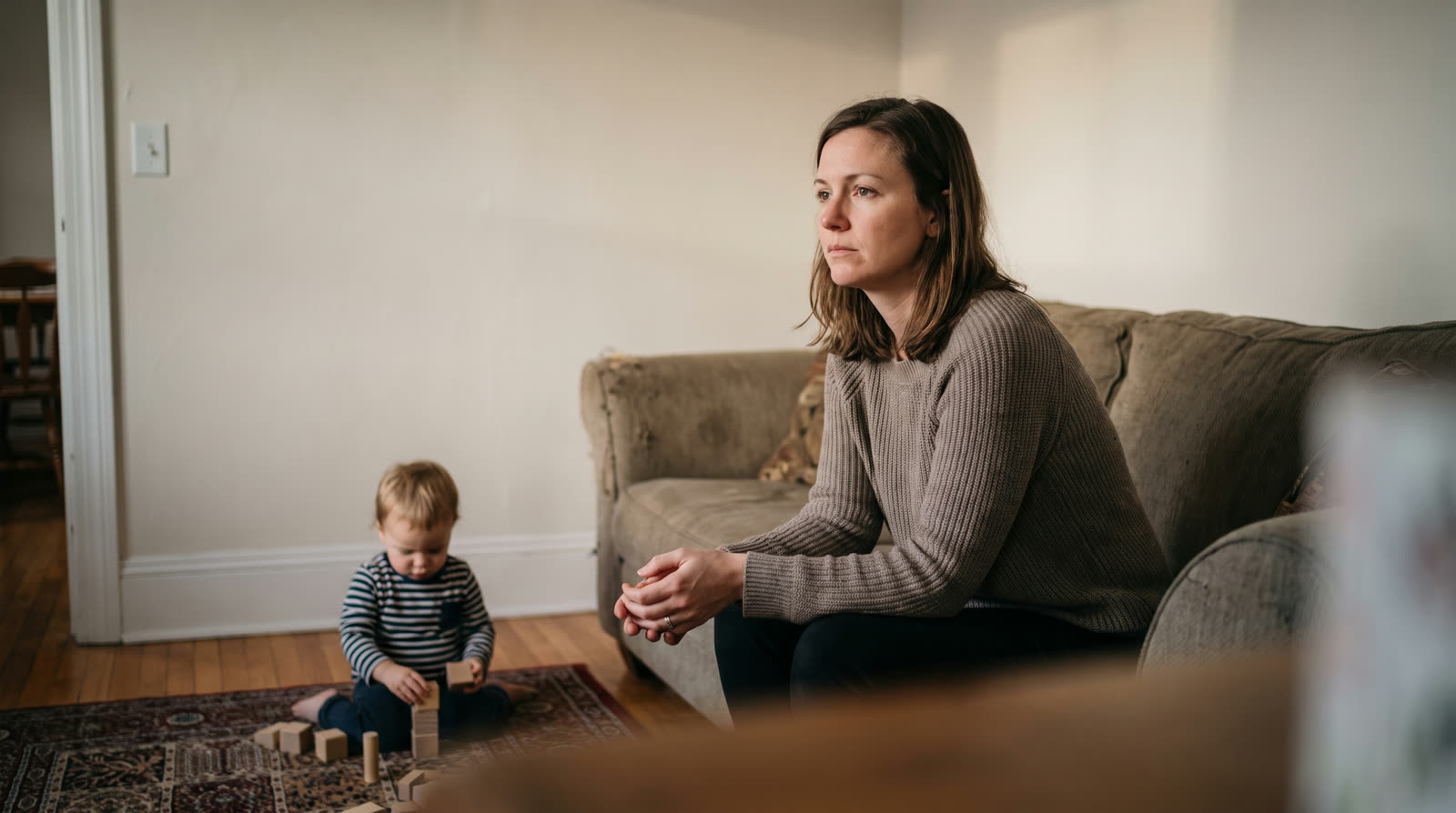 Mother sitting on a couch while her toddler plays nearby